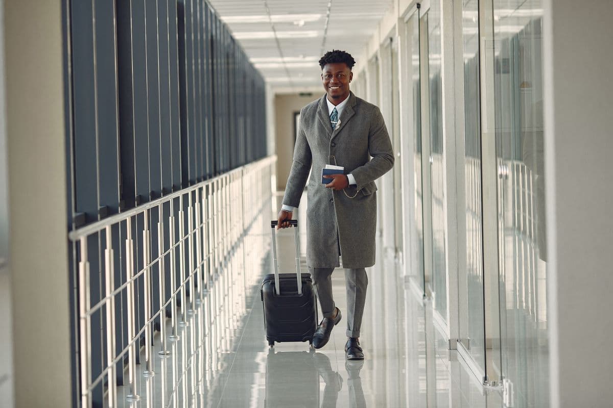 Business traveler in a coat rolling a suitcase through a bright airport corridor