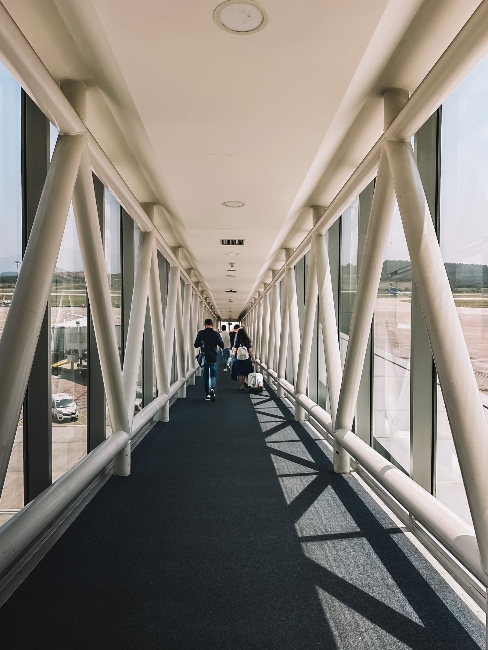 Travelers walking down a sunlit airport jet bridge toward their gate