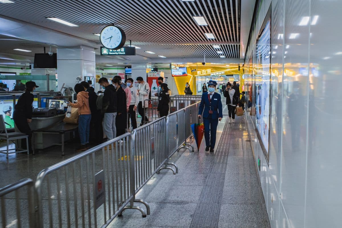 Travelers queuing at an airport security checkpoint behind a barrier line