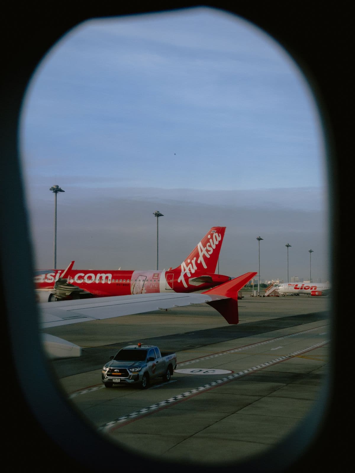 AirAsia aircraft viewed from a plane window at Don Mueang Airport, Bangkok, during sunset