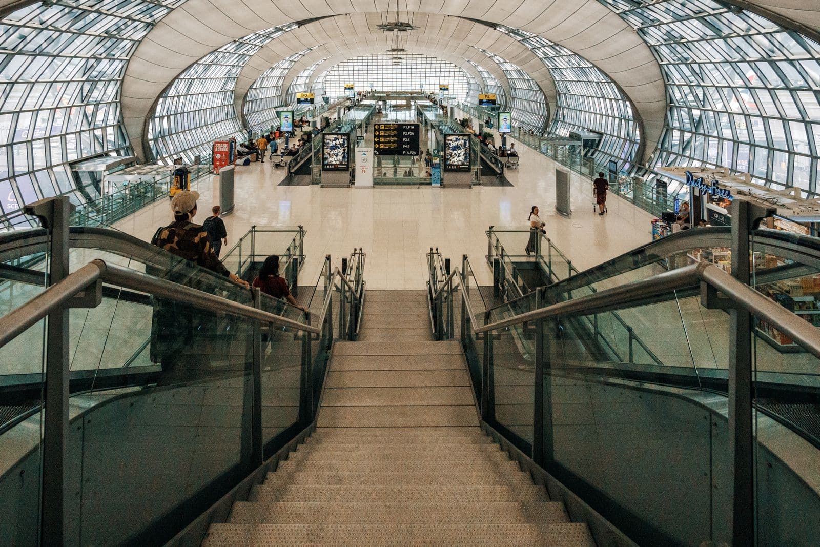 Sweeping staircase beneath a curved glass terminal roof at a modern international airport